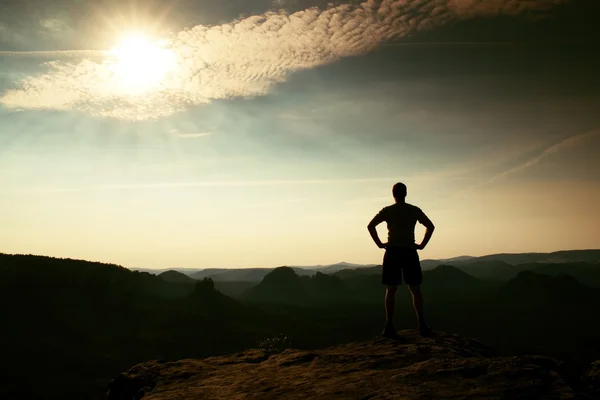 Man in shirt and pants on cliff  of sandstone rock in national park Saxony Switzerland and watching over the misty and foggy morning valley to Sun. — Stockfoto