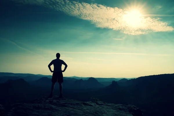 Uomo in camicia e pantaloni sulla scogliera di roccia arenaria nel parco nazionale della Sassonia Svizzera e guardando la nebbiosa e nebbiosa valle del mattino al sole . — Foto Stock