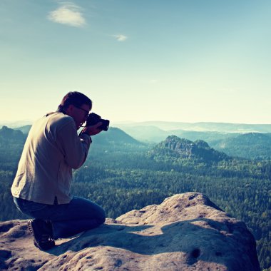 Siyah saçlı adam fotoğraf büyük ayna kamera dağ tepe üzerinde boynundaki güneş doğarken alıyor.