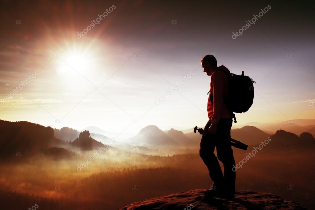 Silhouette of photographer overlooking a blanket of fog over valley to sun