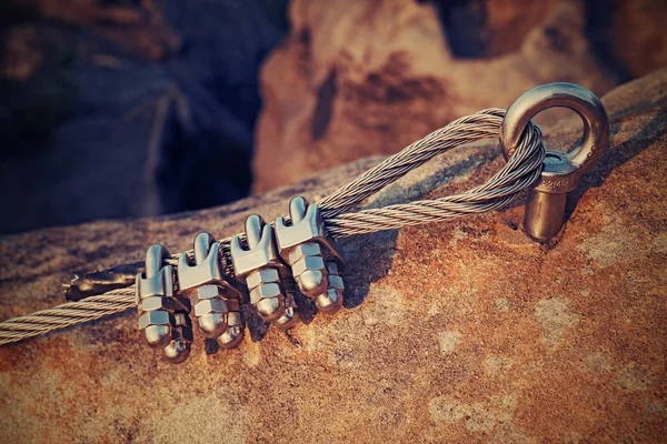 Solid knot on steel rope. Iron twisted rope fixed in block by screws snap hooks. Detail of rope end anchored into sandstone rock — Stock Photo, Image