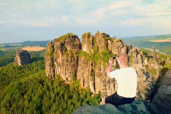 Uçurum rock ve alır fotoğraf peyzaj feryat akıllı telefon kısa saçlı adam. Güneşli bir günde rocky Dağları — Stok fotoğraf