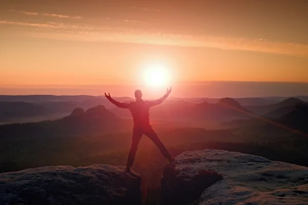 Caminhante de salto em preto comemorar triunfo entre dois picos rochosos. Maravilhoso amanhecer com o sol acima da cabeça .. — Fotografia de Stock