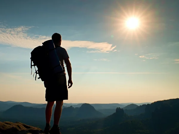 Turista alto com postes na mão. Noite ensolarada em montanhas rochosas. Caminhante com grande mochila no ponto de vista rochoso acima do vale nebuloso. Efeito de vinheta . — Fotografia de Stock