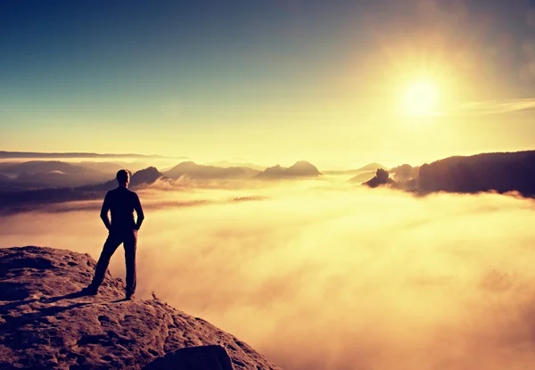 Hiker in black stands on rock abve valley within daybreak and watch to Sun. Beautiful moment the miracle of nature — Stock Photo, Image