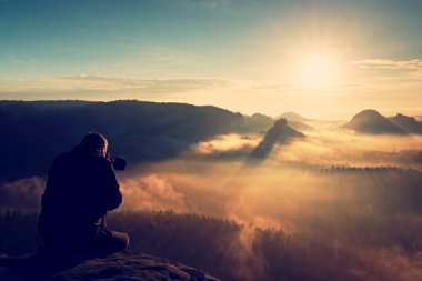 Bulutların üstünde profesyonel fotoğrafçı silueti, sisli dağlar.
