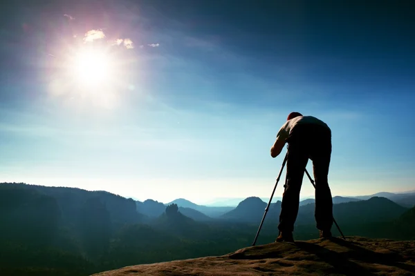 Foto-Enthusiasten bleiben mit Stativ auf Klippe und denken. verträumte Nebellandschaft, blauer nebliger Sonnenaufgang in einem wunderschönen Tal unten — Stockfoto