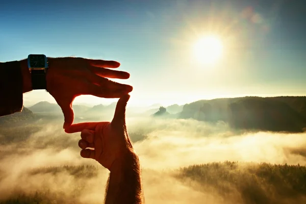 Nahaufnahme von Händen, die eine Rahmengeste machen. blauer Nebel unter felsigen Gipfeln. sonniger Frühlinganbruch in nebligen felsigen Bergen. — Stockfoto