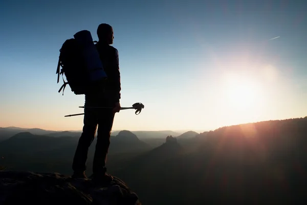 Tall backpacker with poles in hand. Sunny hike day in rocky mountains. Hiker with big backpack stand on rocky view point above misty valley. — Stock Photo, Image