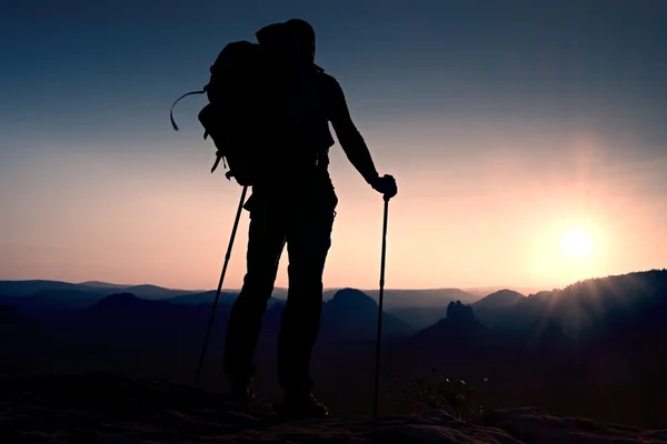 Tall backpacker with poles in hand. Sunny hike day in rocky mountains. Hiker with big backpack stand on rocky view point above misty valley. — Stock Photo, Image