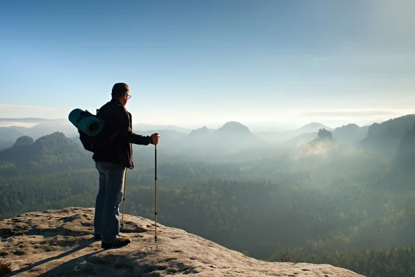 Pro batůžkáře s brýle a holí v ruce. Slunečný den v rocky mountains. Tramp s velkým batohem na skalnaté pohledu bod nad mlhavé údolí. — Stock fotografie