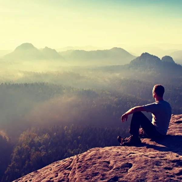 Caminante de pelo corto alto en camisa ligera sentarse en una roca y disfrutar de paisajes de montaña brumosos —  Fotos de Stock