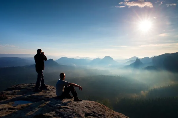 Randonneurs et passionnés de photo restent avec trépied sur la falaise et la pensée. Paysage brouillard rêveur, lever de soleil bleu brumeux dans une belle vallée en contrebas — Photo