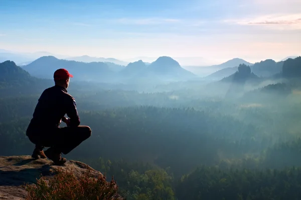 Runner in red cap and  in dark sportswear in squatting position  enjoy mountain scenery — Stock Photo, Image