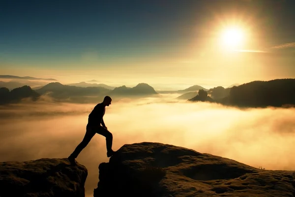 Pazzo escursionista in nero sta saltando tra le cime rocciose. Splendido sorgere del giorno in montagne rocciose, nebbia pesante nella valle profonda. Miracolo della natura — Foto Stock