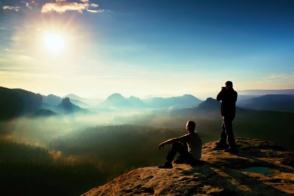 ハイカーと写真愛好家は崖と考え三脚をと一緒に。美しい渓谷の下で夢のような濃霧発生風景、青い霧日の出 — ストック写真