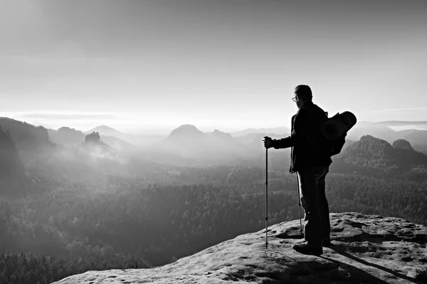 Backpacker mit Brille und Stöcken in der Hand. sonniger Tag in den felsigen Bergen. Wanderer mit großem Rucksack auf felsigem Aussichtspunkt über nebligem Tal. — Stockfoto