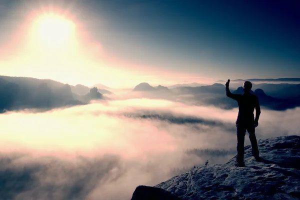 Hiker is taking photo by smart phone on peak of mountain at sunrise. — Stock fotografie