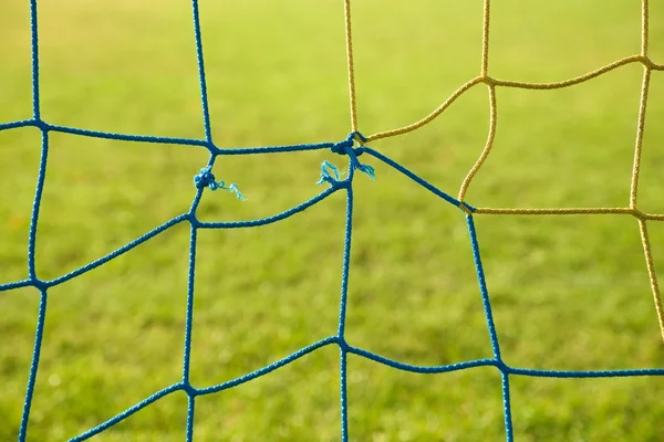Detalle de redes de fútbol cruzadas azules amarillas, fútbol fútbol en la red de portería con césped pobre en el patio de recreo en el fondo . —  Fotos de Stock