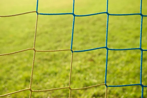 Detalhe de amarelo azul cruzado redes de futebol, futebol em gol net com grama pobre no playground no fundo . — Fotografia de Stock