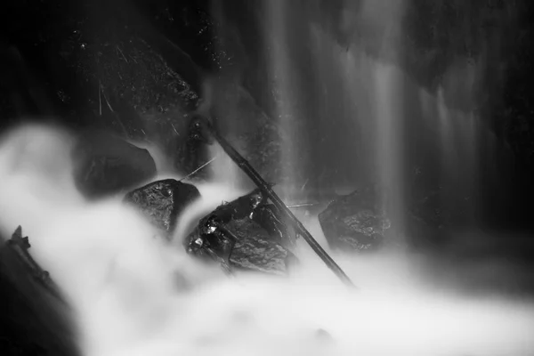 Pulvérisation d'eau sous une petite cascade sur un ruisseau de montagne, l'eau tombe sur un rocher mousseux. Le spray crée sur le niveau et le gravier de l'eau laiteuse. Branches et troncs cassés dans l'eau — Photo