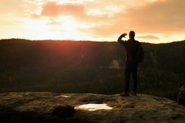 Turist kılavuz kutup ile yolda elinde. Uzun yürüyüşe çıkan kimse sportif sırt çantası ile kayalık Görünüm noktası puslu Vadisi üzerinde durmak. Güneşli bahar daybreak kayalarda