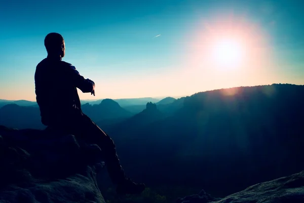 Turisztikai kivenni egy kis pihenést. Csinos, fiatal férfi ült a sziklán, és élvezi a kilátás a ködös Sziklás-hegység. — Stock Fotó