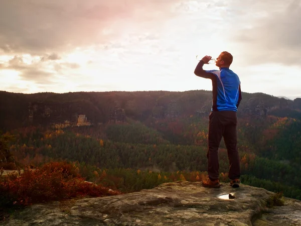 Thirsty hiker in blue and black sportswear with bottle of water. Sweaty tired tourist on the peak of sandstone rocky park