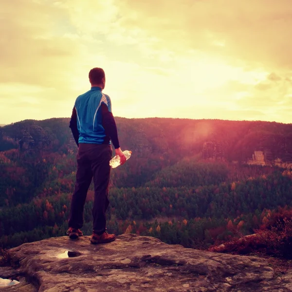 Sweaty tall hiker in cyan trikot with bottle of water. Adult tired tourist on the peak of rock watch into misty landscape. — Stock Photo, Image