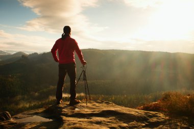 Tripod üzerinde cliff ve düşünme ile doğa fotoğrafçısı. Rüya gibi adamlara manzara, turuncu puslu gündoğumu Valley aşağıdaki