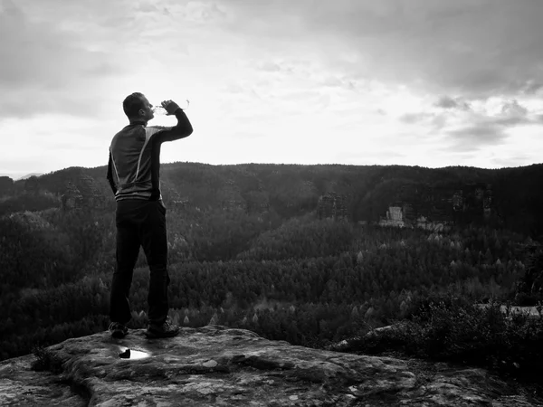 Durstige Wanderer in blauer und schwarzer Sportbekleidung mit Wasserflasche. schwitzmüder Tourist auf dem Gipfel des Sandsteinfelsenparks — Stockfoto