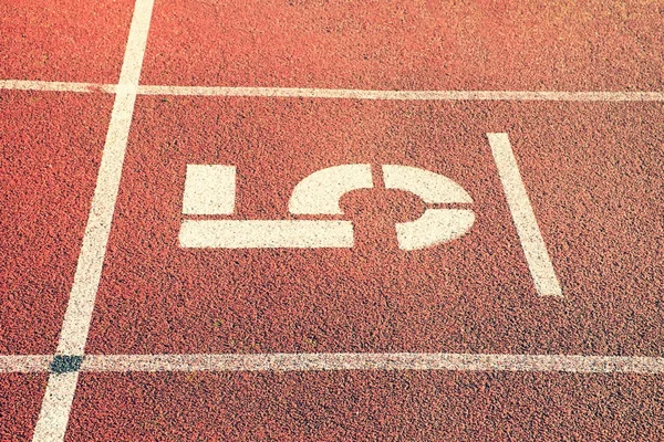 Číslo pět. Velké bílé číslo na červené gumové závodiště. Jemně texturované běžící závodiště v atletický stadion. — Stock fotografie