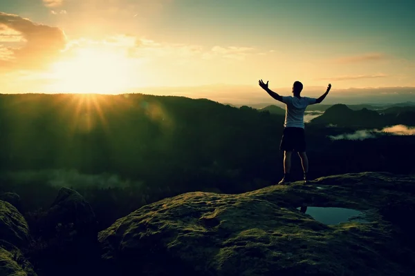 Runner on the peak. Man in his target gesture triumph with hands in the air. Crazy man in black pants and white cotton t-shirt,