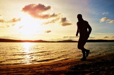 Uzun boylu adam sunglass ve karanlık kap sonbahar gün batımında sahilde çalışıyor