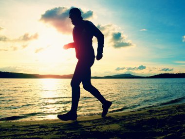 Uzun boylu adam sunglass ve karanlık kap sonbahar gün batımında sahilde çalışıyor