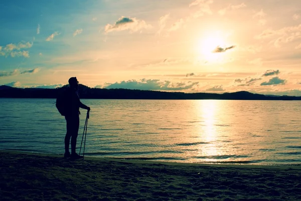 Caminhante homem de sportswear escuro e com mochila desportiva em pé na praia, relaxar e desfrutar do pôr do sol no horizonte. Dia mágico do outono . — Fotografia de Stock