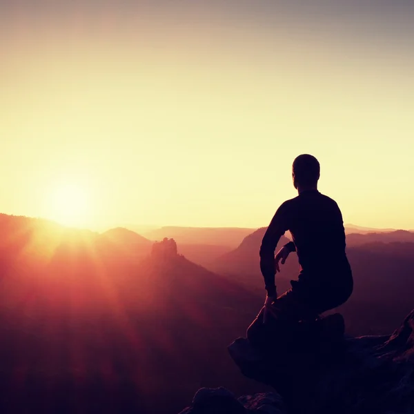 Man tourist sit finally on peak of mountain. Travel mountain scene. Sun at horizon — Stock Photo, Image