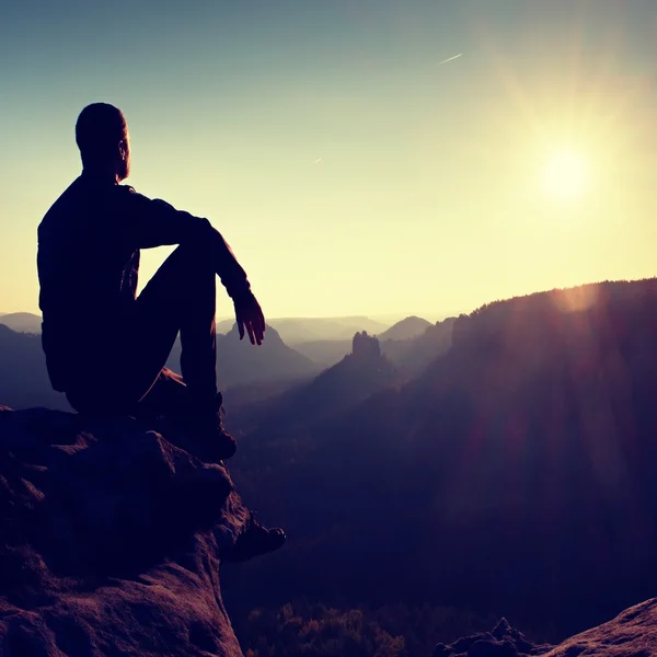 Homem turista sentar-se finalmente no pico da montanha. Cena de montanha de viagem. Sol no horizonte — Fotografia de Stock
