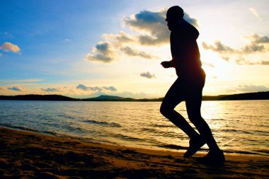 Siluet spor etkin adam çalıştıran ve canlı renkli batımında sahilde egzersiz.