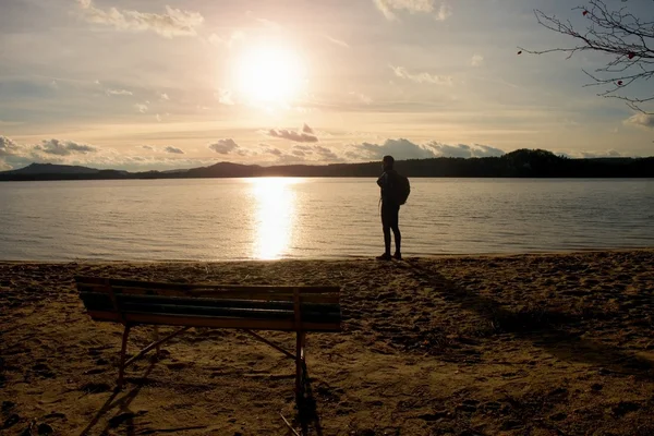 Tall man goes to lake coast near old wooden empty bench. Vintage toned photo — Stock Photo, Image