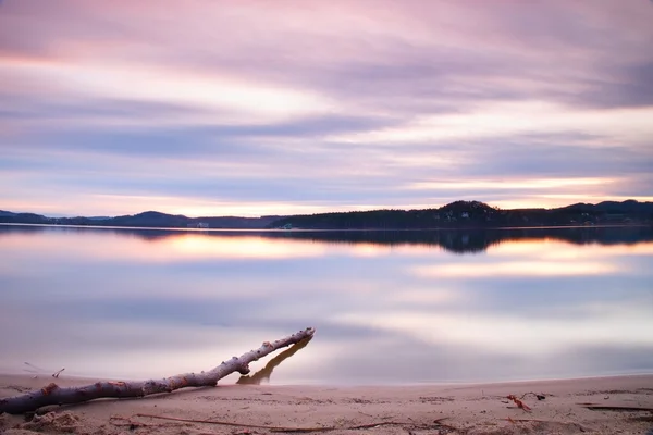 Lange Belichtung des Seeufers mit abgestorbenem Baumstamm, der nach Sonnenuntergang ins Wasser gefallen ist. — Stockfoto