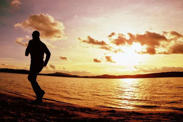 Ψηλός αθλητικός τύπος που τρέχει κατά μήκος ακτή της θάλασσας της Ανατολή του ηλίου πίσω από, άδειο παραλία — Φωτογραφία Αρχείου