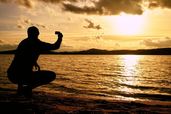 Grand homme prenant des photos du coucher du soleil avec téléphone portable. Jour d'automne au bord de la mer — Photo