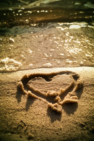 Прекрасное маленькое сердце, зарисованное соленым песком на пляже. Вечерние теплые цвета зеркала заката на уровне воды . — стоковое фото