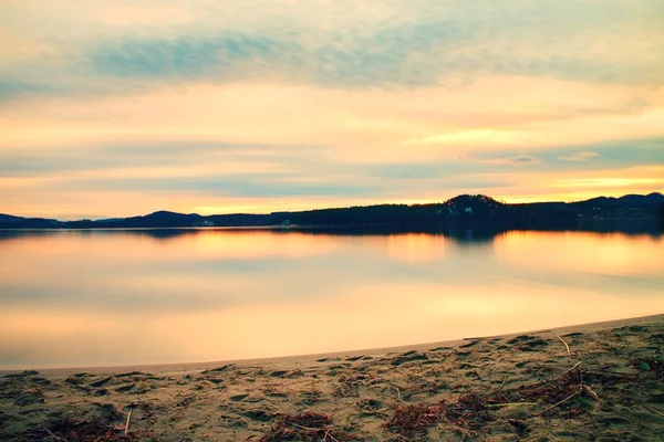 Verlassener Sandstrand am See vor dem Sonnenuntergang im Herbst, Sonnenstrahlen zwischen Wolken und Spiegelungen im Wasserspiegel — Stockfoto