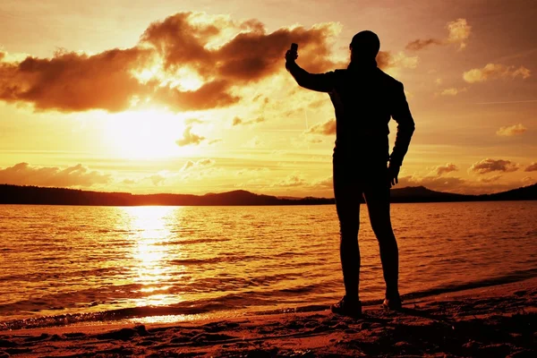 Wysoki mężczyzna robienia zdjęć zachodu słońca z telefonu komórkowego. Jesienny dzień w wybrzeże Morza — Zdjęcie stockowe