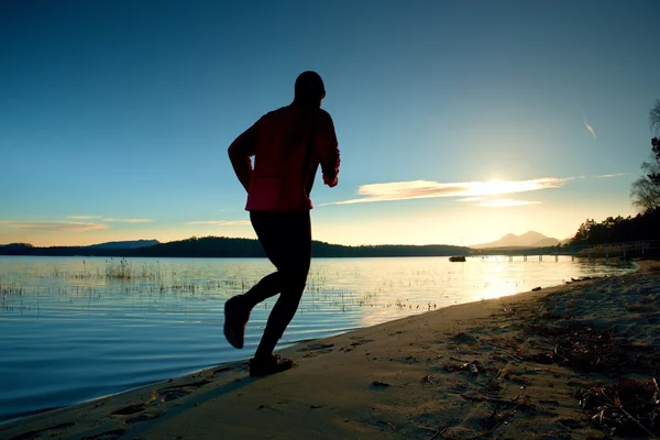 Sportowy człowiek robi Jogging rano na plaży w jasny świt sylwetki — Zdjęcie stockowe