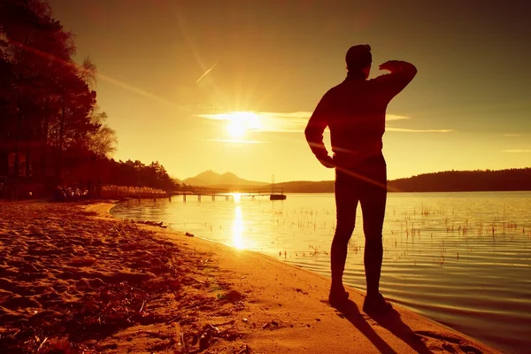 Silhouet van de persoon op een daling zien uit de zon. Slanke sportman op strand shadowing ogen . — Stockfoto