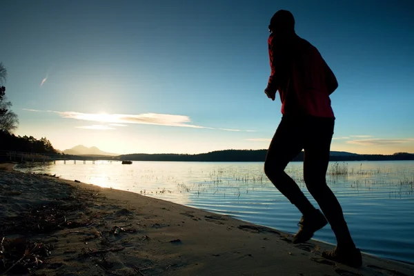 Sportowy człowiek robi Jogging rano na plaży w jasny świt sylwetki — Zdjęcie stockowe