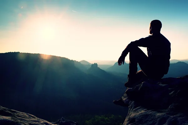 Турист отдыхает. Красивый молодой человек сидит на скале и наслаждается видом на туманные скалистые горы . — стоковое фото